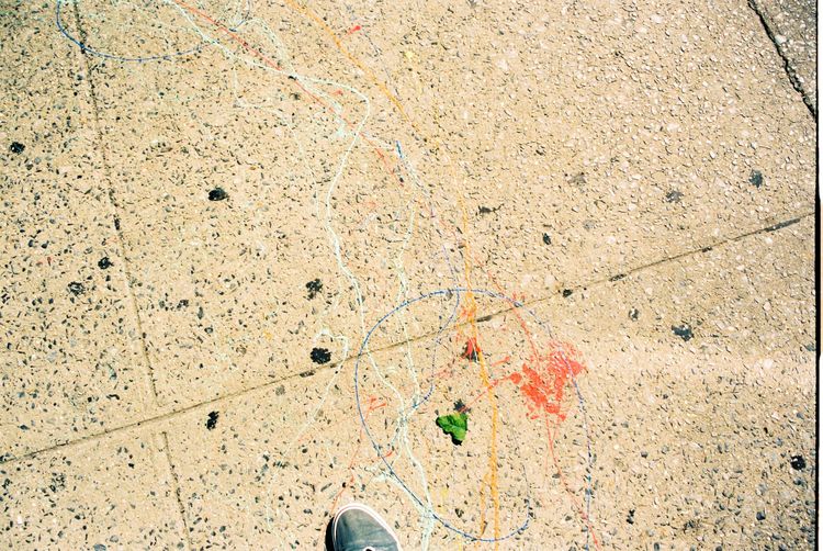 Downward view of the photographer's sneaker on pavement marked with colorful dripped paint squiggles.