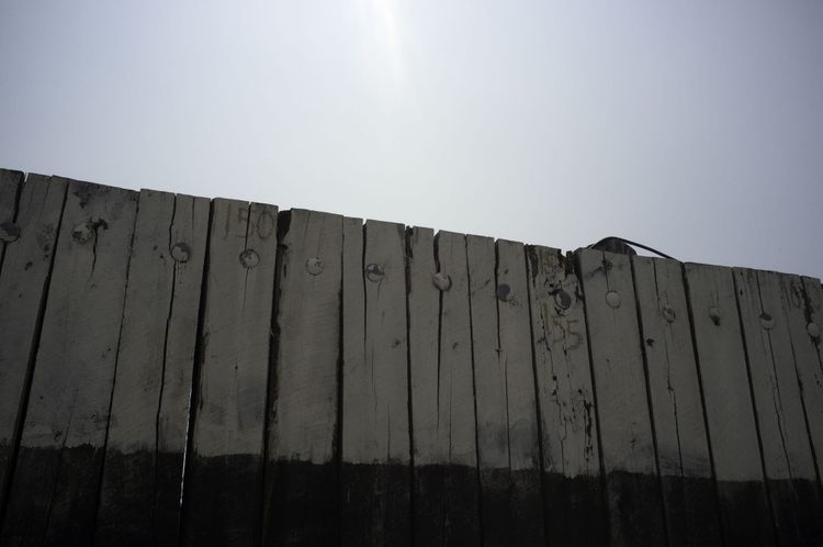 Weathered wooden ferry pier wall painted white and black with heavy metal bolts against a blue sky.