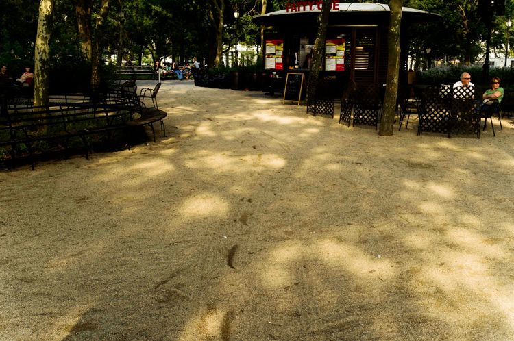 Dappled sunlight over the Fatty 'Cue food kiosk at Battery Park Beer Garden with outdoor patrons.