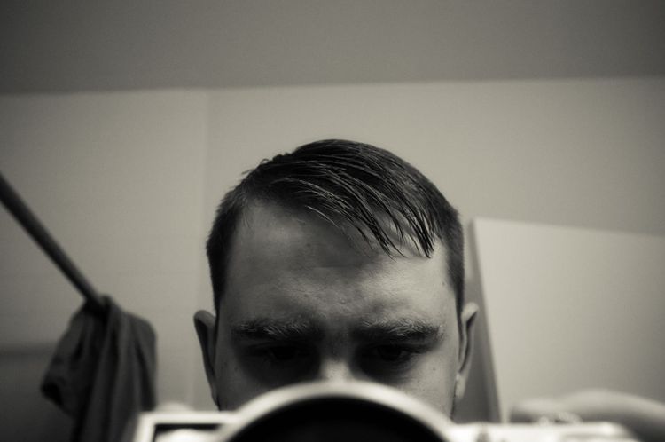 Black and white mirror selfie holding a camera showing overgrown hair before a haircut.