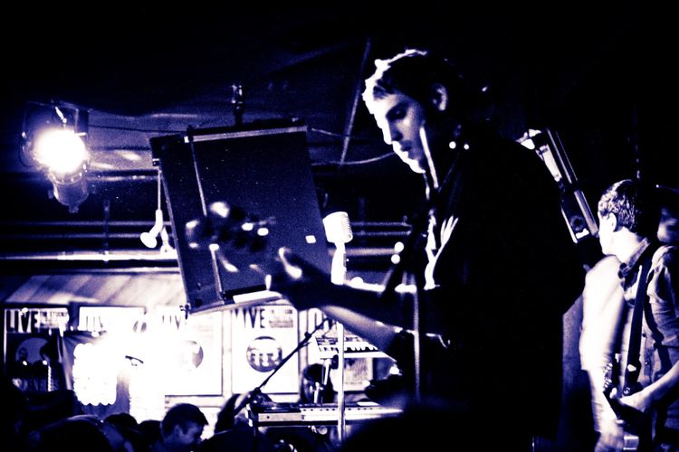 Guitar effects pedals and tangled audio cables across the wooden stage floor at a concert.
