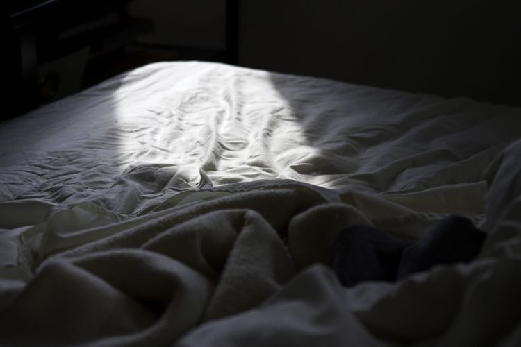 Morning sunlight washing across rumpled white bed sheets and duvet.