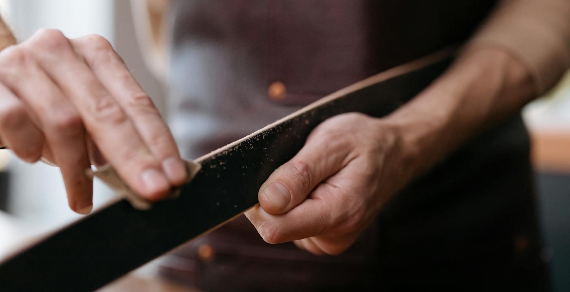 Handwerker bearbeitet die Lederkante eines Gürtels in einer Werkstatt