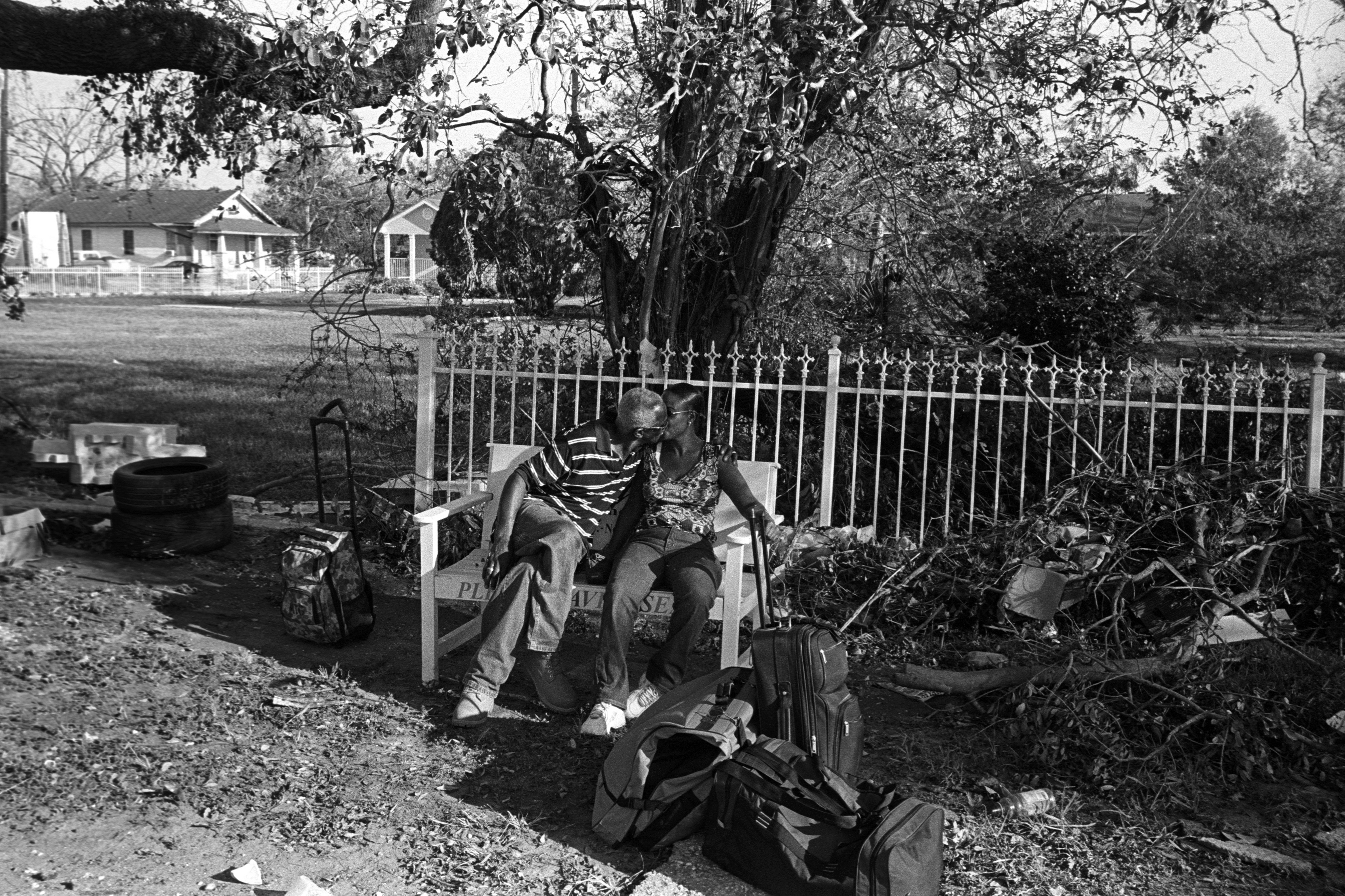 "We Made It." New Orleans, 2005. Inkjet Print on Canvas. Photographed in the aftermath of Hurricane Katrina, this image captures a couple seated on a bench, sharing a kiss amid packed luggage and storm debris. Having survived the flood and displacement, they chose to marry, affirming love as both anchor and act of resilience. In the midst of ruin, their embrace testifies to the power of intimacy, commitment and hope to endure beyond catastrophe. This image stands as a quiet counterpoint to loss, revealing how even in devastation, love insists on a future. Credit: Clarence Williams