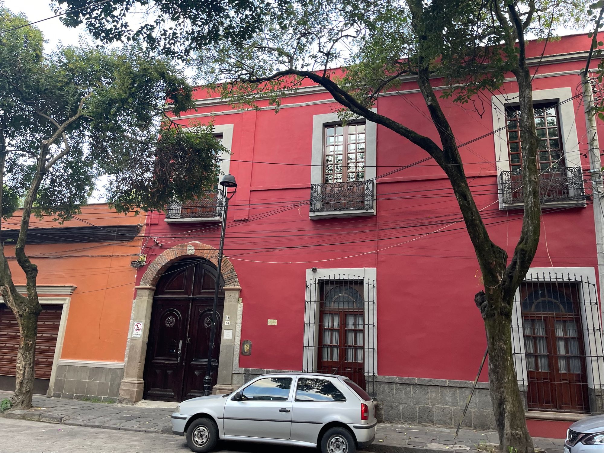 Red house in coacyacan with 3 doors, 3 windows, car in front, cement.