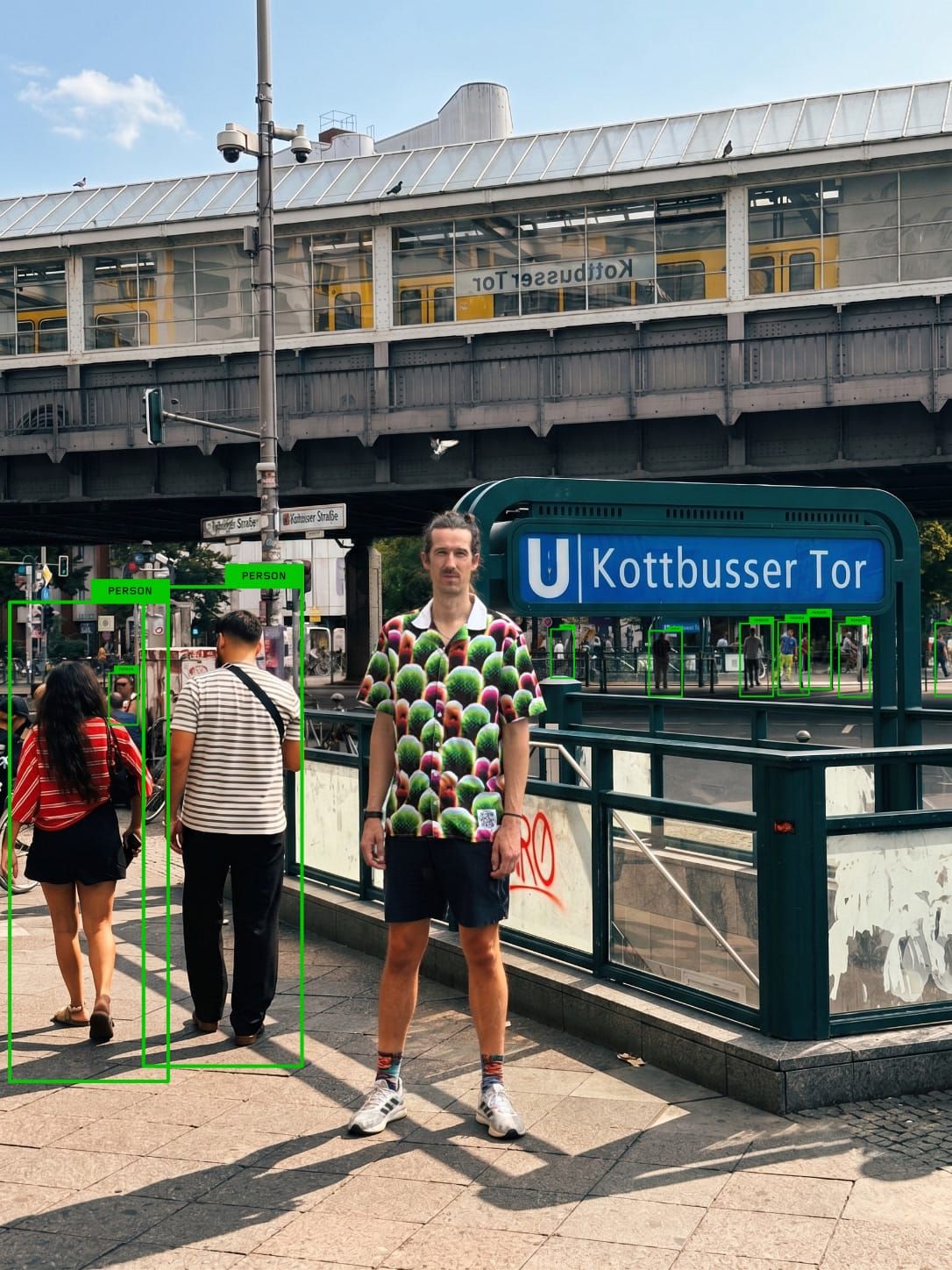 Simon Weckert 穿著 Digital Camouflage 襯衫站在 Kottbusser Tor，YOLO 標出周圍行人但沒有標記他