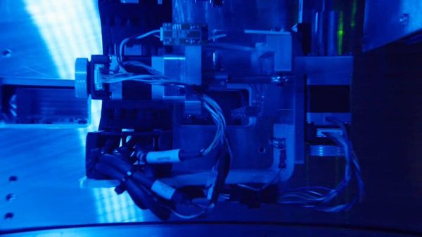 Atomic Machines 官方製造設備展示，畫面呈現藍色照明下的機械與管線