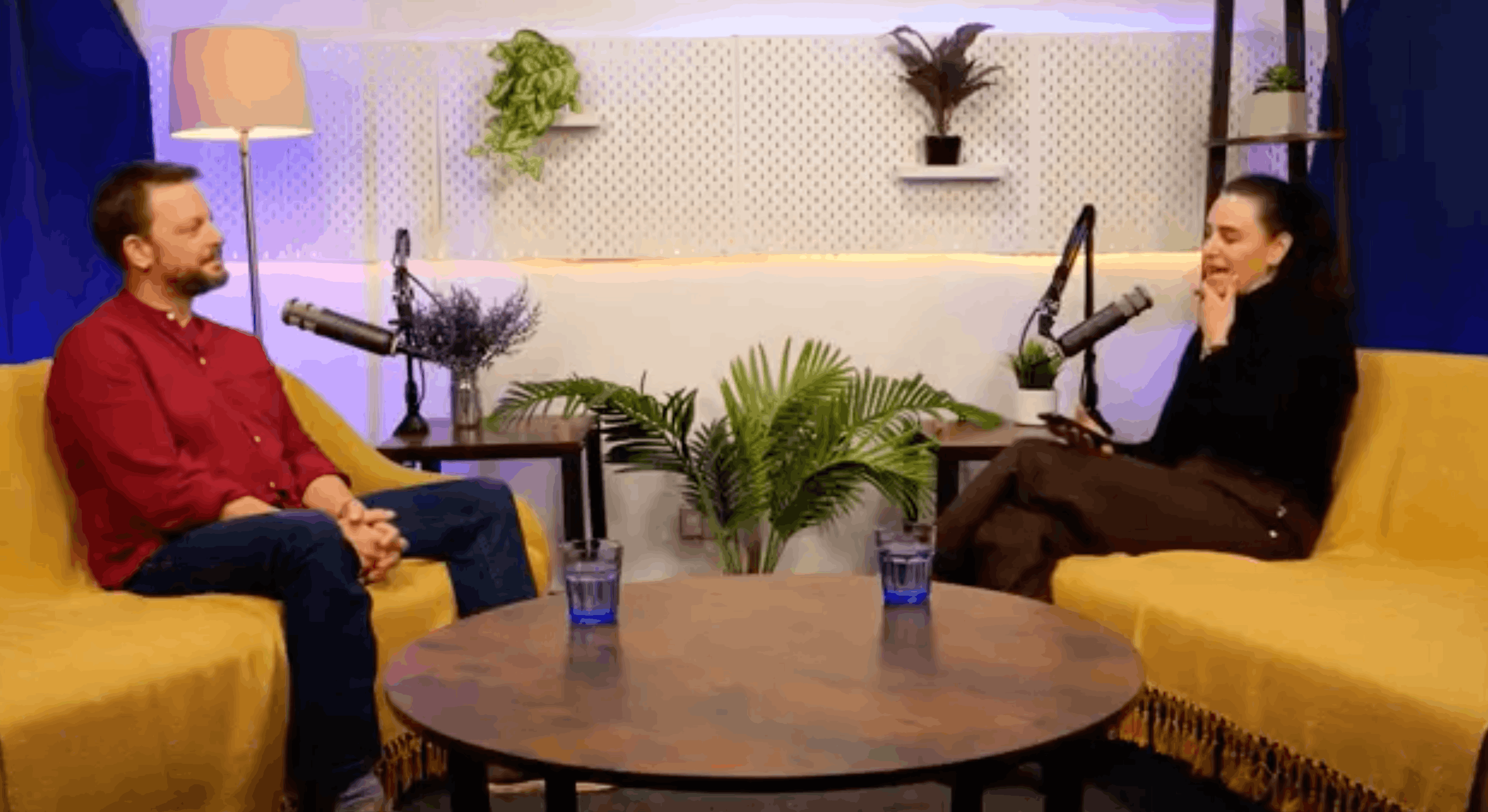 Matthew Matheson in a red shirt and host Aleksandra King in conversation on the BEYOND set, seated on yellow sofas either side of a round wooden table