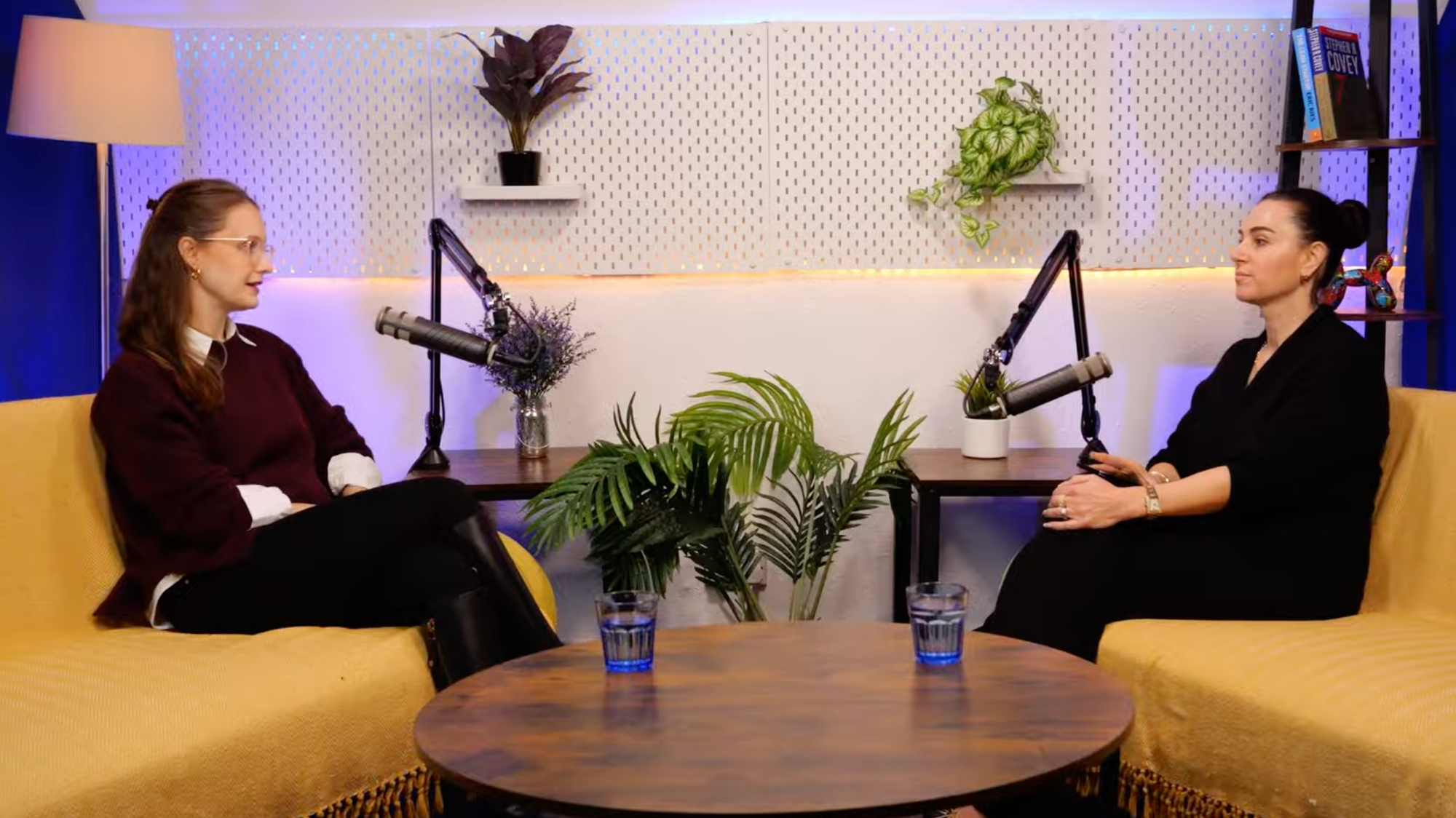 Jessica Cath in a burgundy jumper and host Aleksandra King in conversation on the BEYOND set, seated on yellow sofas either side of a round wooden table