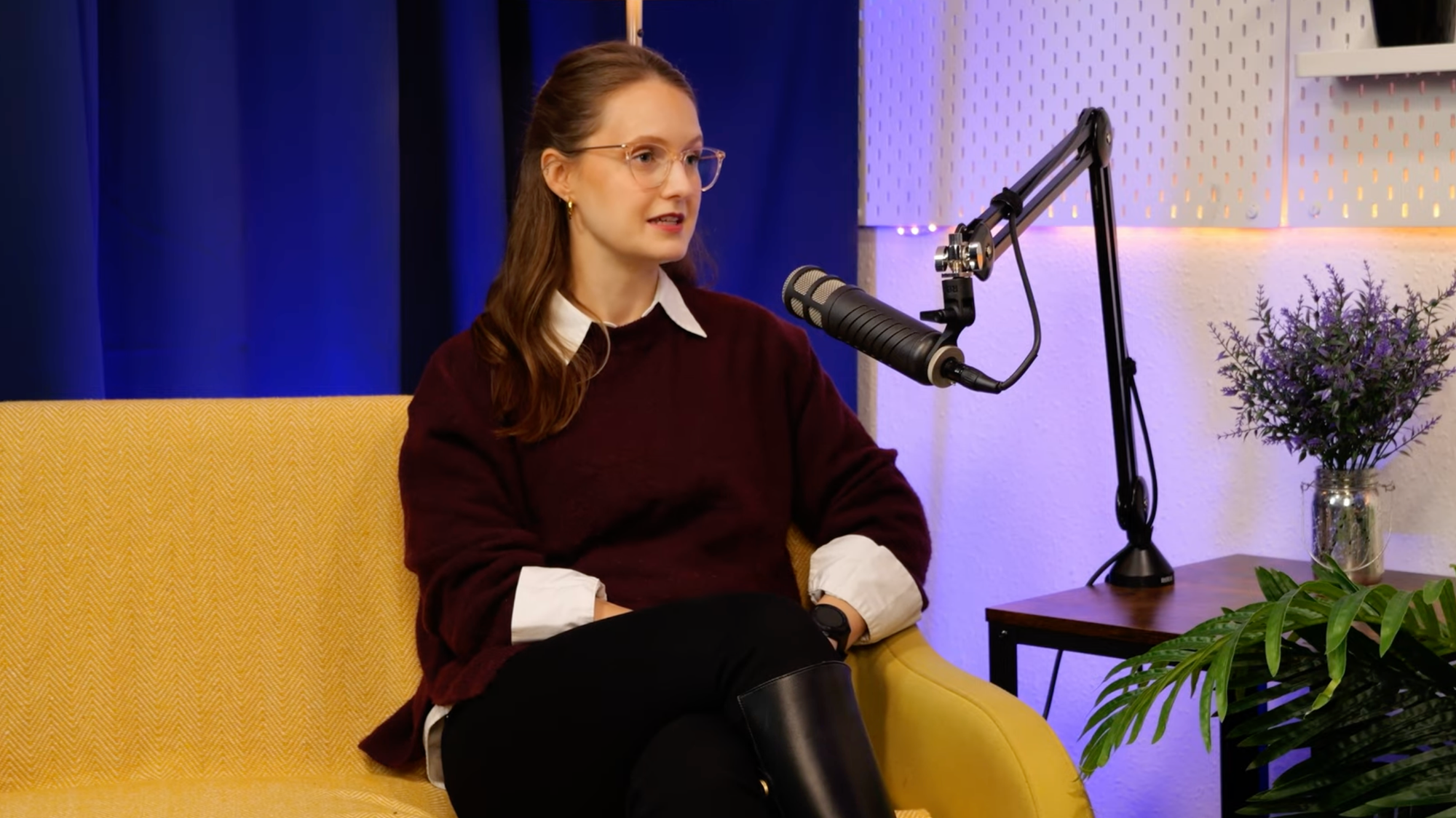 Jessica Cath speaking at the microphone during her BEYOND interview, in glasses and a burgundy jumper over a white collared shirt