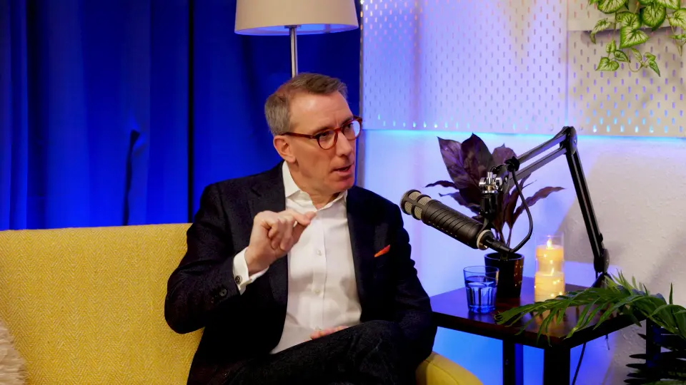 Geoff White making a point during his BEYOND interview, hand raised, podcast microphone beside him