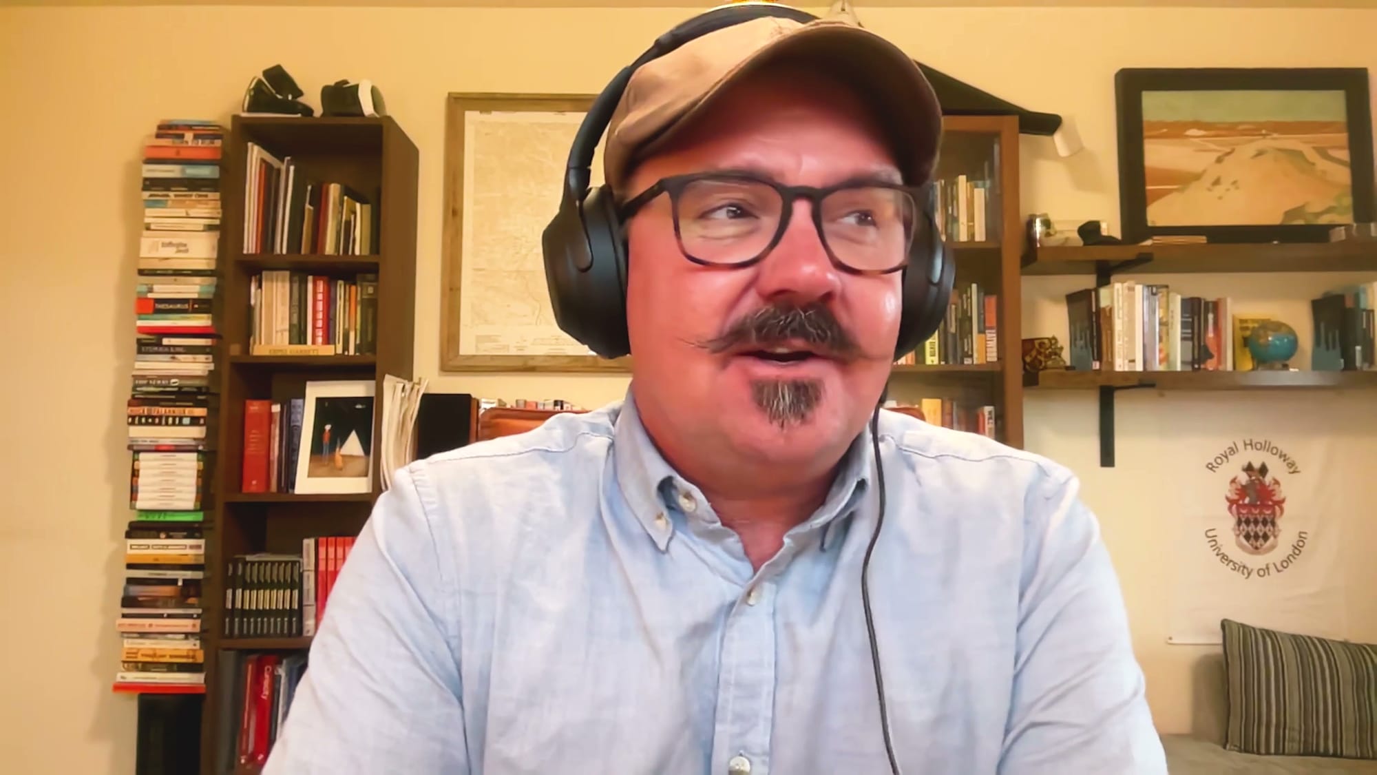 Bradley Garrett in cap and headphones speaking on The BEYOND Podcast from his book-lined study in the Mojave Desert