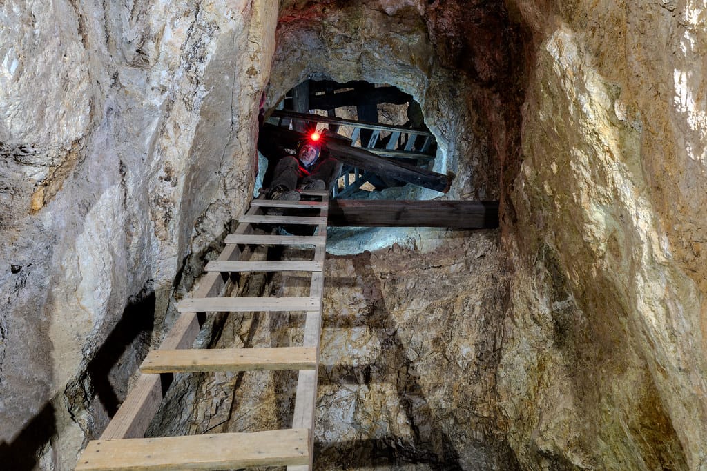 A wooden ladder rising through a rocky passage in an abandoned mine, an explorer's red light glowing at the top– photographed by Bradley Garrett