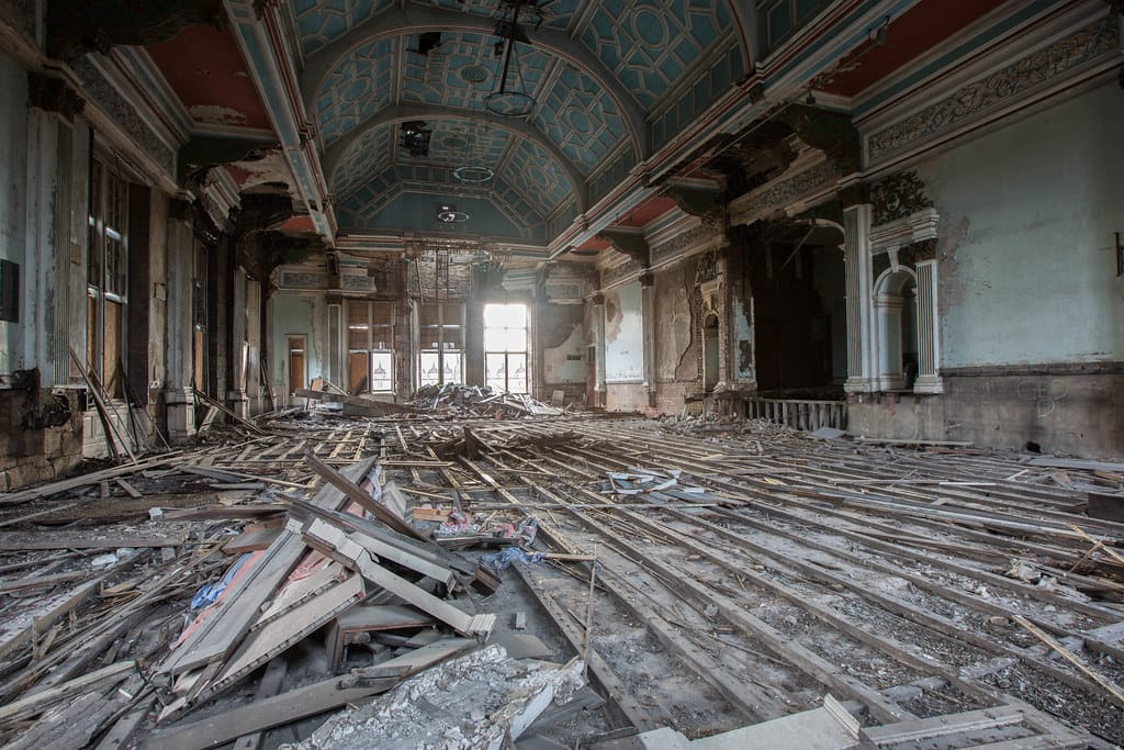 The derelict great hall of an abandoned building with its floorboards torn up and collapsing, photographed by Bradley Garrett