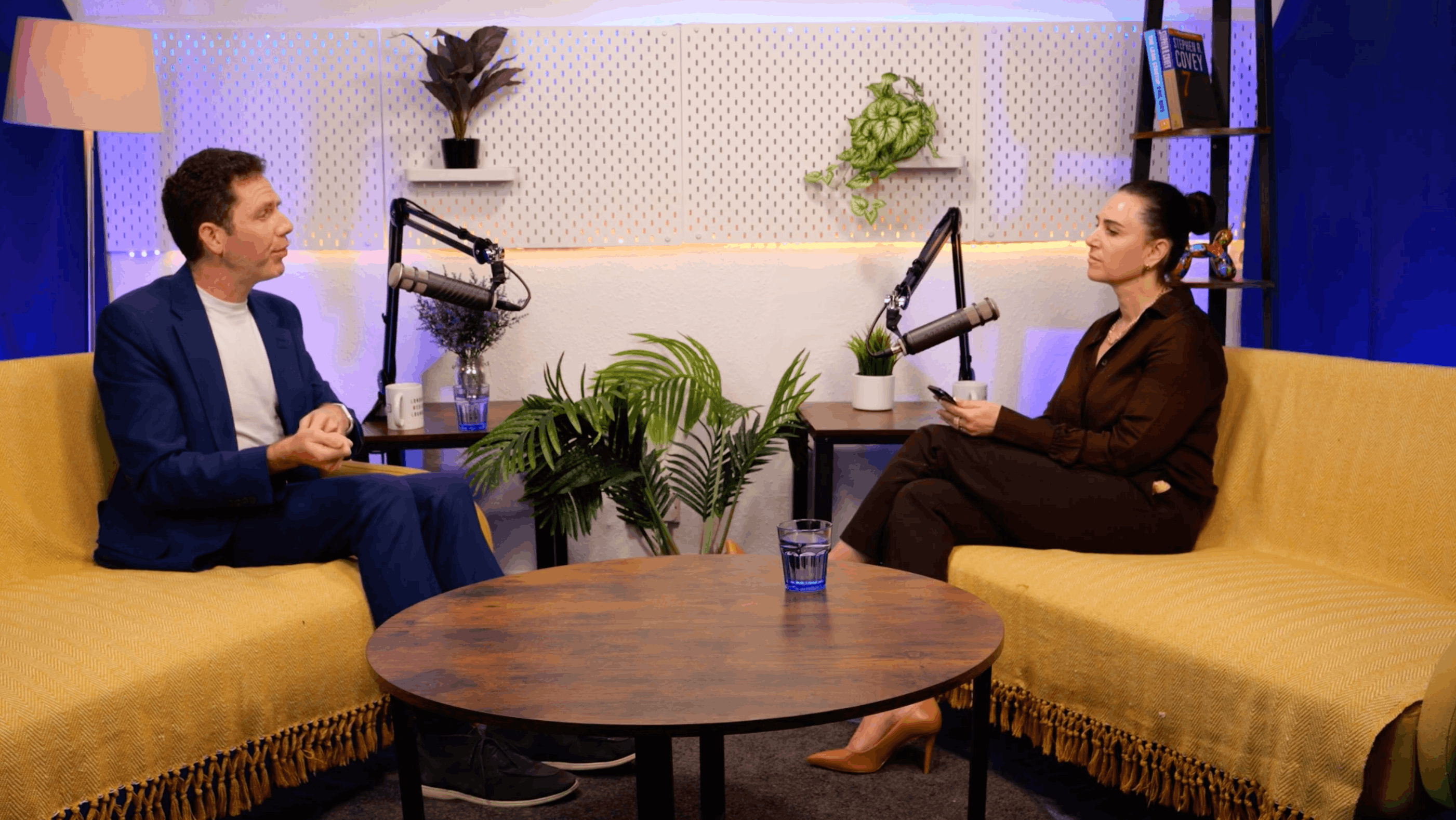 David Robson in a blue suit and host Aleksandra King in conversation on the BEYOND set, seated on yellow sofas either side of a round wooden table