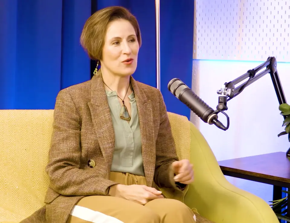 Emma Taylor in a tweed blazer speaking on the BEYOND set, boom microphone in frame