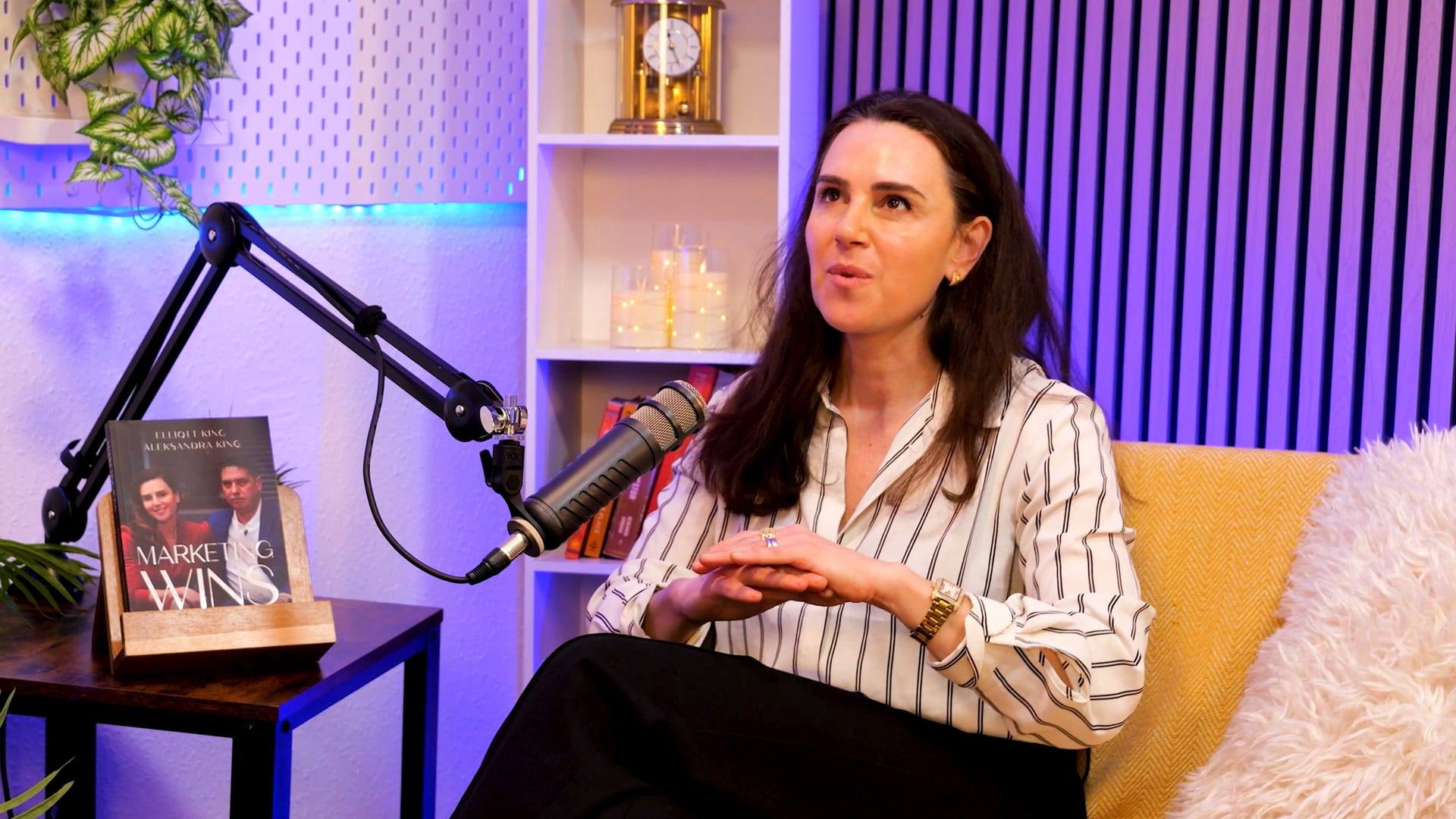 Aleksandra King in a striped shirt, smiling with her hands clasped beside a studio microphone