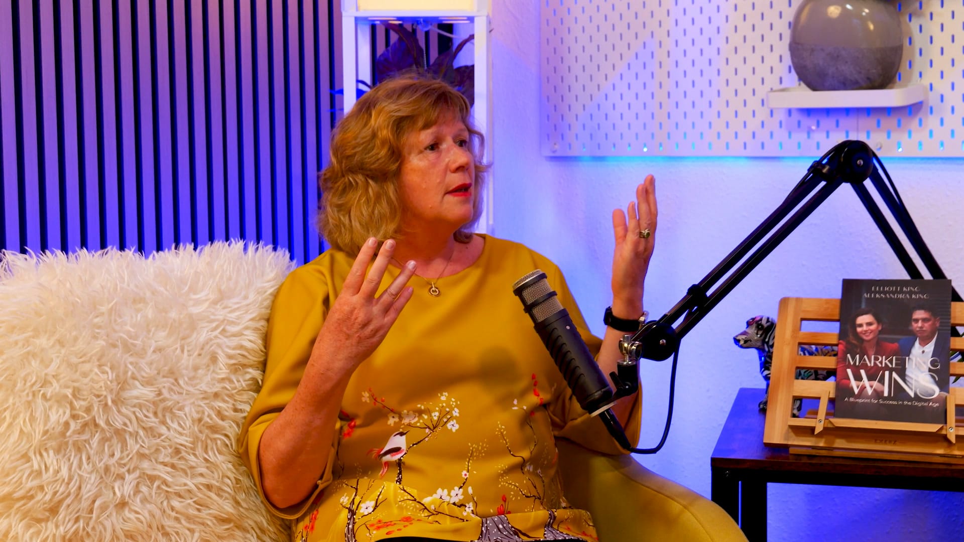 Sue Stockdale gesturing with both hands as she tells a story on The BEYOND Podcast set