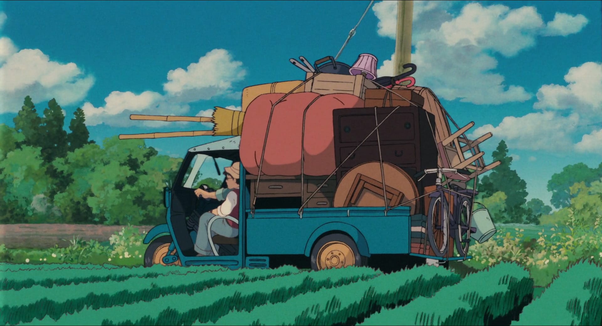 Shot from My Neighbor Totoro of the family truck, loaded up with their things for the new house, driving through a farm field.