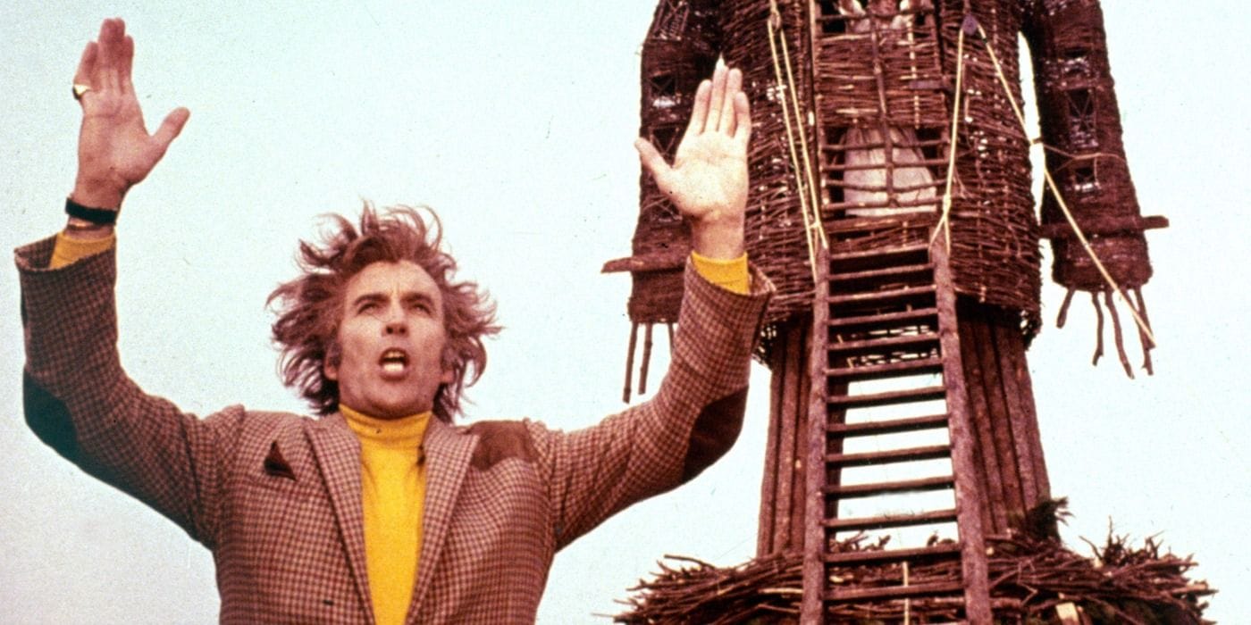 Christopher Lee as Lord Summerisle in The Wicker Man, standing with arms raised in front of The Wicker Man.