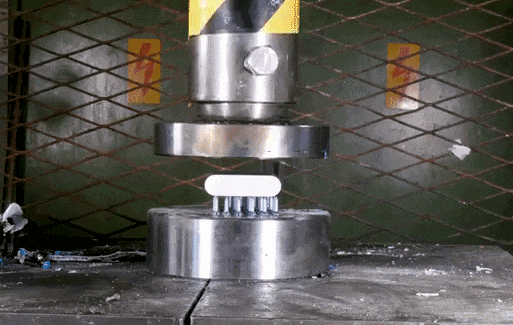 Animated GIF of a pneumatic press crushing a computer component that catches fire and explodes.