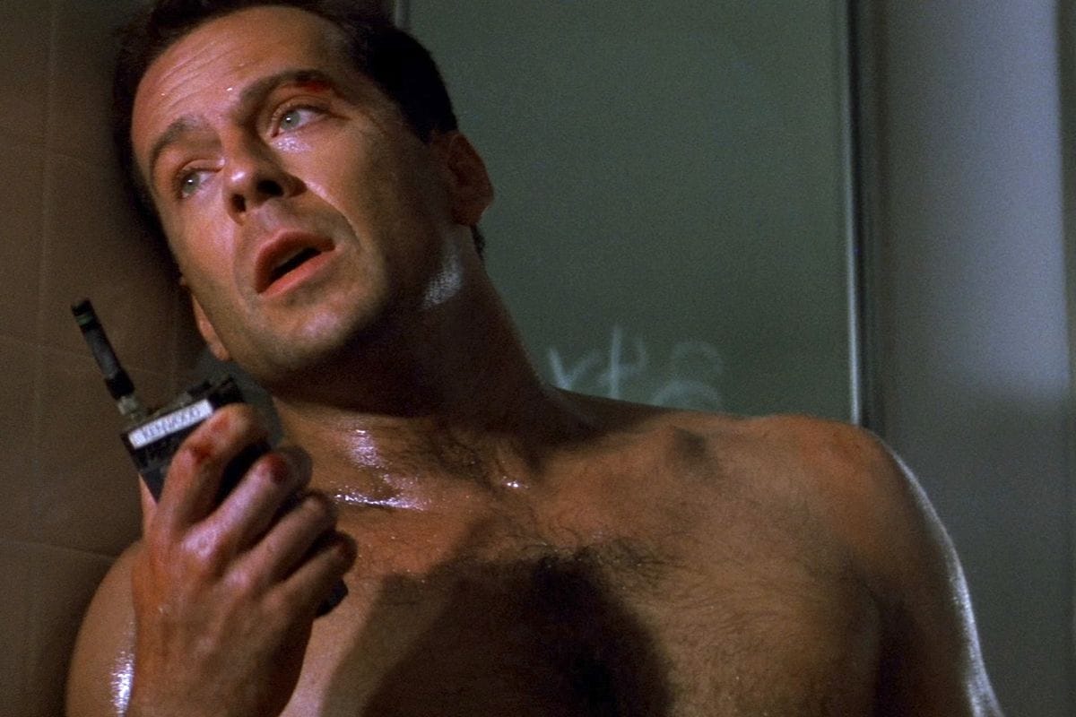 Still from Die Hard: John McClaine, shirtless, speaks into a walkie talkie and looks into the middle distance.