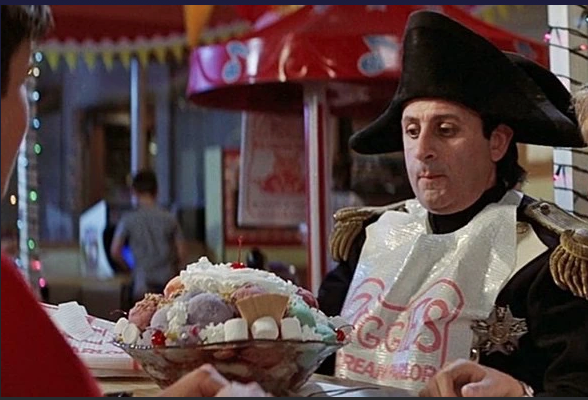 Bill & Ted's Excellent Adventure: Napoleon in a plastic bib stares at a massive trough of ice cream, whipped cream, and marshmallows on the table in front of him.