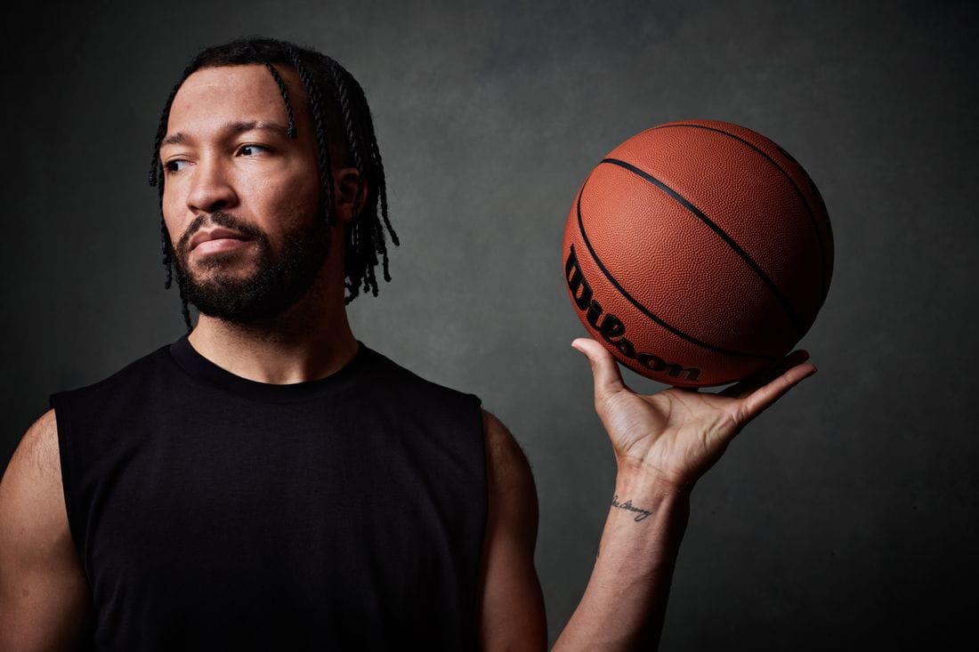 Close Up photo of Jalen Brunson in a photography studio looking to the side holding a basketball with one hand.