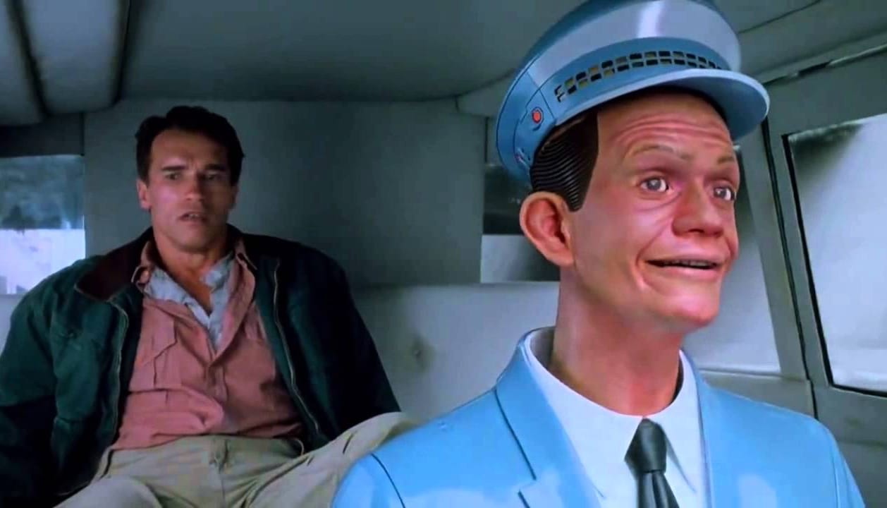 Total Recall: Quaid sits in the back of a Johnny Cab, where the automaton driver looks forward with a cheery expression.