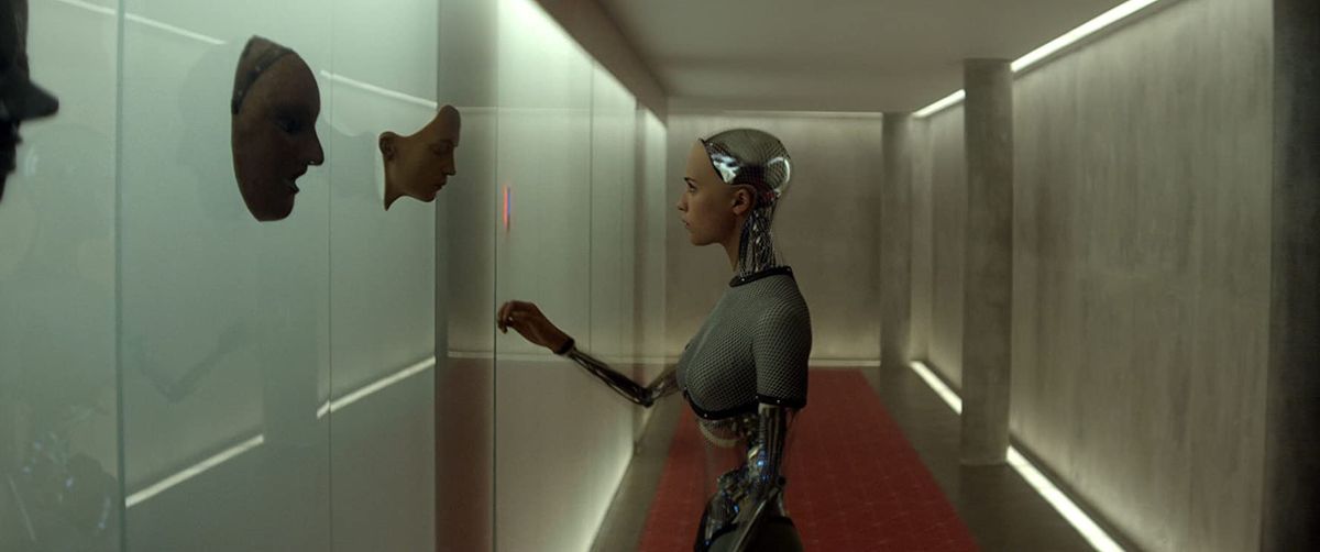 A robot woman examines an artificial face in a hallway, from the movie Ex Machina