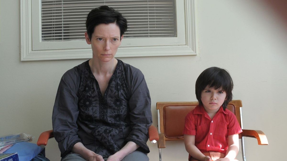 Tilda Swinton sits sullen next to a small boy with a similar expression in We Need to Talk About Kevin
