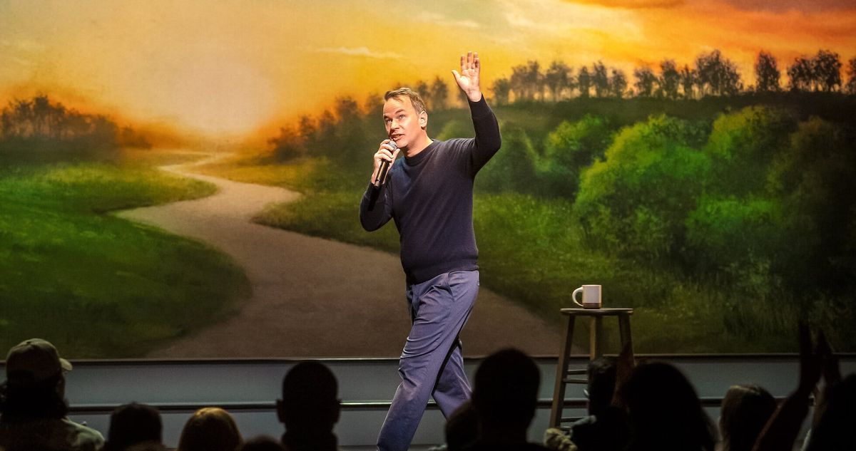 Mike Birbiglia walks onstage, a stool with a coffee mug on it behind him
