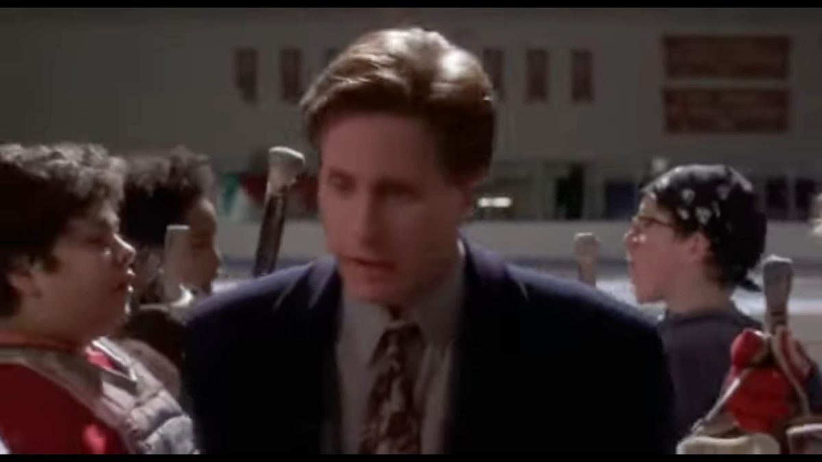 Gordon Bombay in a suit and tie at the hockey rink, walking between two rows of Mighty Ducks.