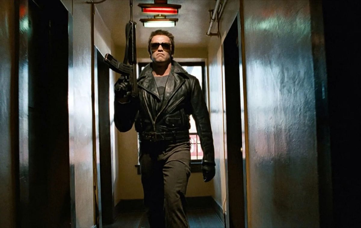 Arnold Schwartzenegger carries a machine gun down a hallway in a still from The Terminator