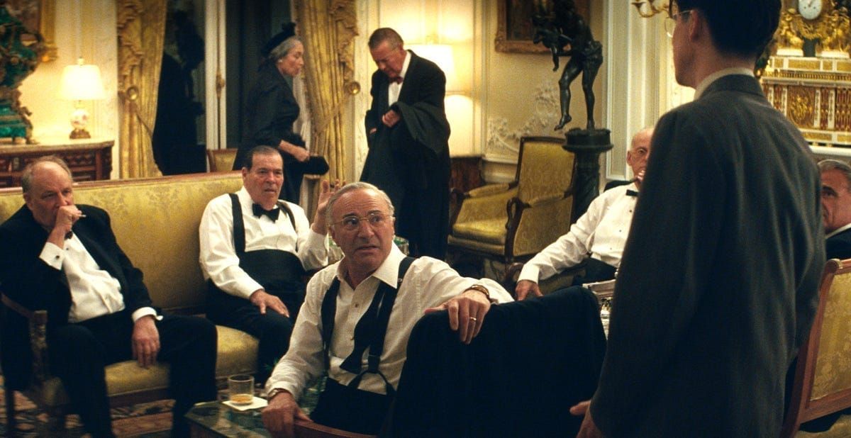 Timothee Chalamet stands in front of a room full of wealthy men in a scene from Marty Supreme