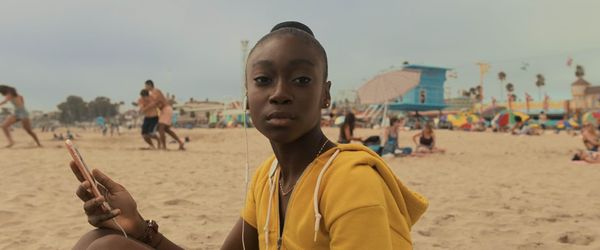 A young girl sits on the beach holding her phone in a still from Jordan Peele'Us.