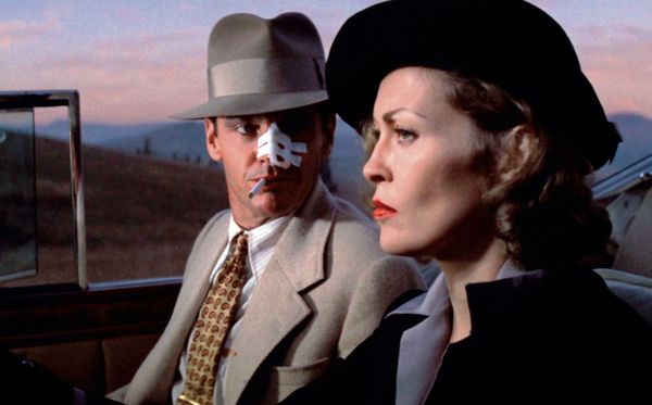 A man with a bandaged face smoking a cigarette sits in the passenger seat of a car being driven by a 1940's woman in a scene from Chinatown