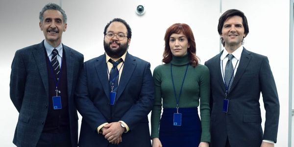 The Innies of Severance taking a group photo in the office with a security camera behind them.