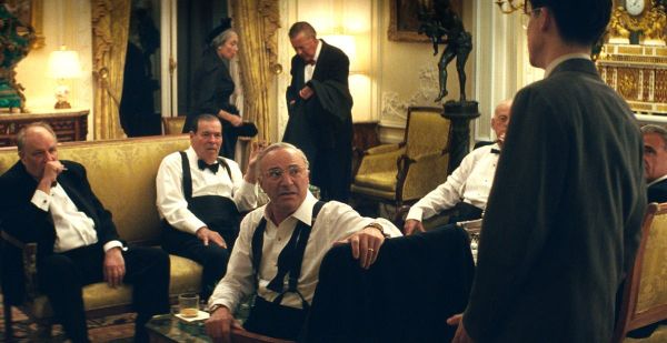 Timothee Chalamet stands in front of a room full of wealthy men in a scene from Marty Supreme