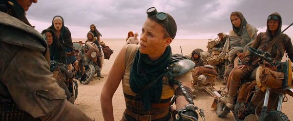 Mad Max Fury Road: A desert dune with a cloudy sky. Over the shoulder shot of Max's shoulder centered on Furiosa, with the Wives and Many Mothers on motorcycles behind her.