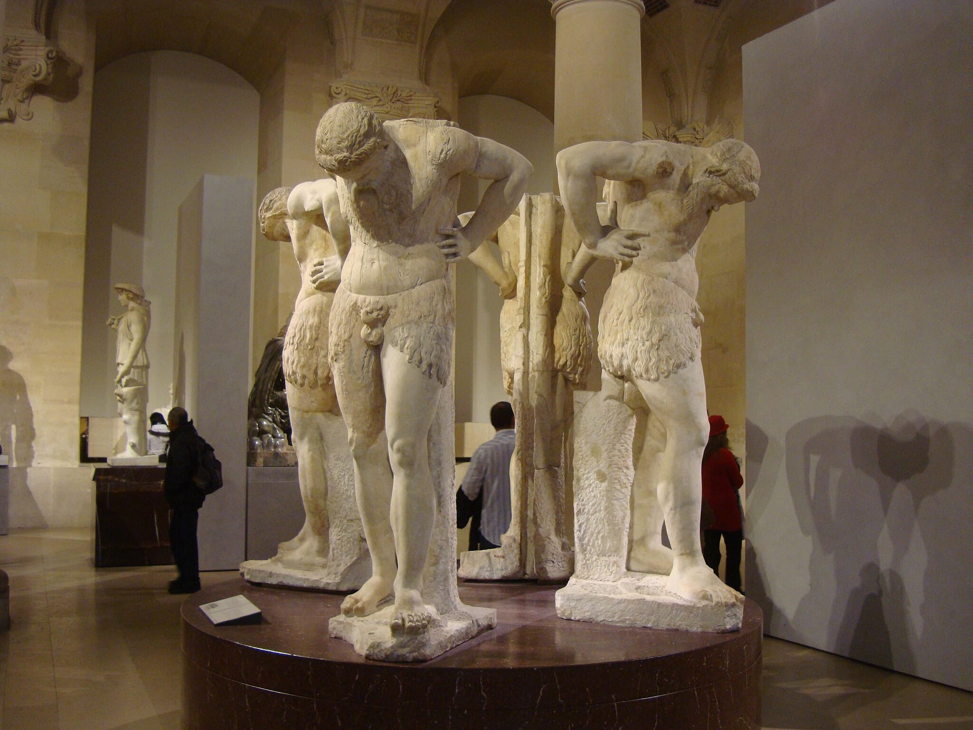 Four large statues of satyrs looking down, all standing in a circle at the Louvre.