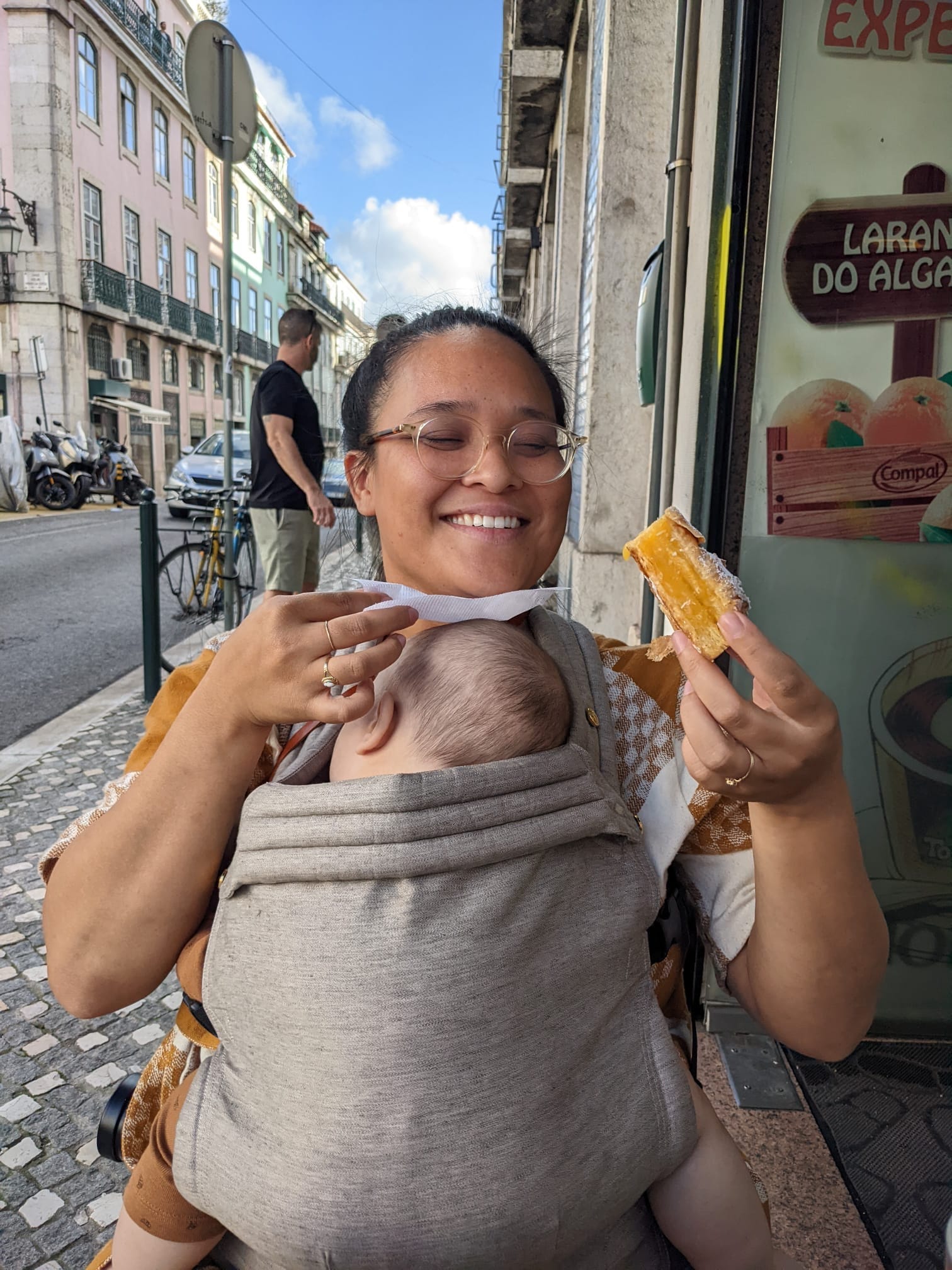On a scenic street in Lisbon, Celeste Noche enjoys a treat while her baby sleeps on her chest.