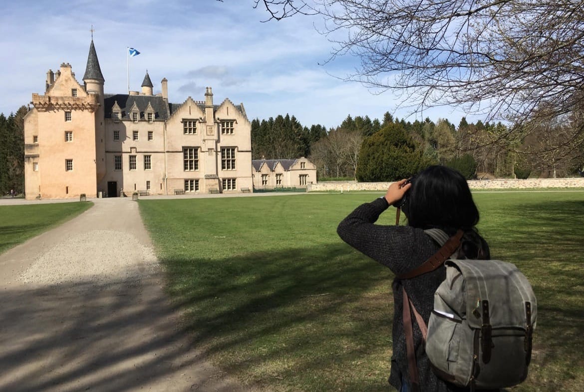 Celeste gazes through the viewfinder of her camera, looking at a castle.