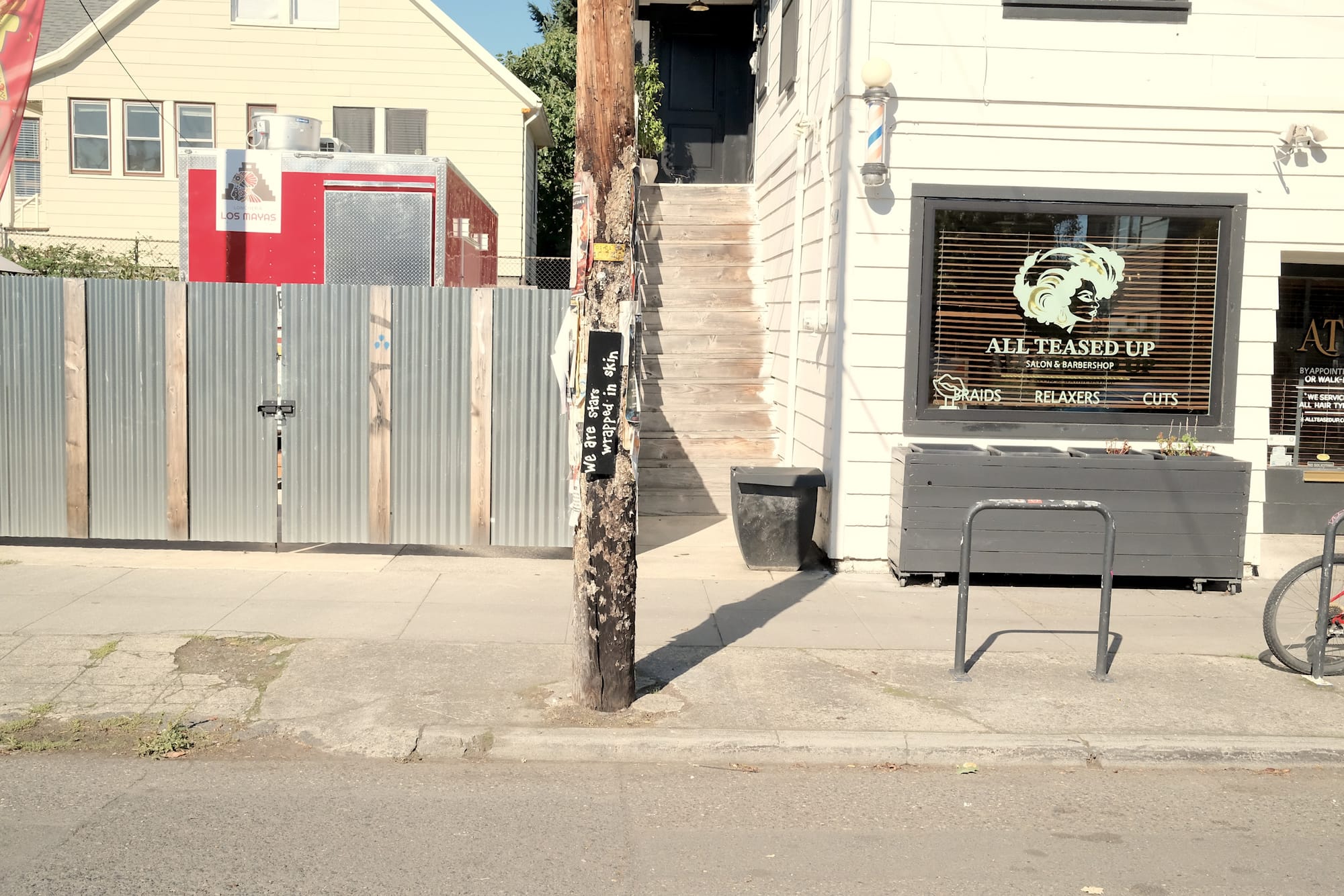 On a utility pole, a sign reads "We are stars wrapped in skin," with food carts and and a salon behind.
