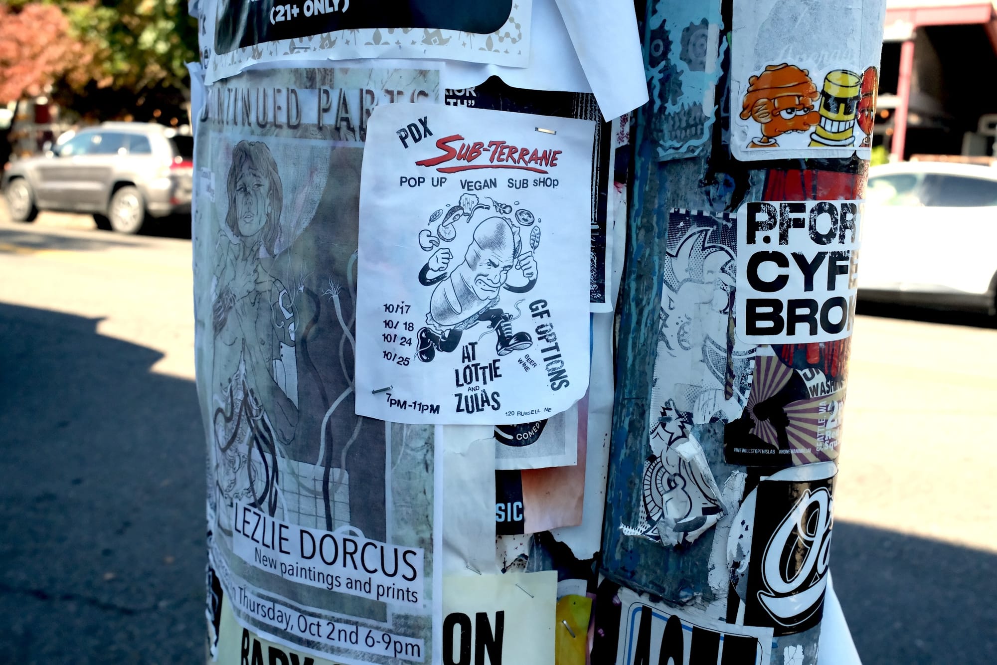 A utility pole with a poster for a vegan sub shop, with a comical illustration of a sandwich with a face and boots.