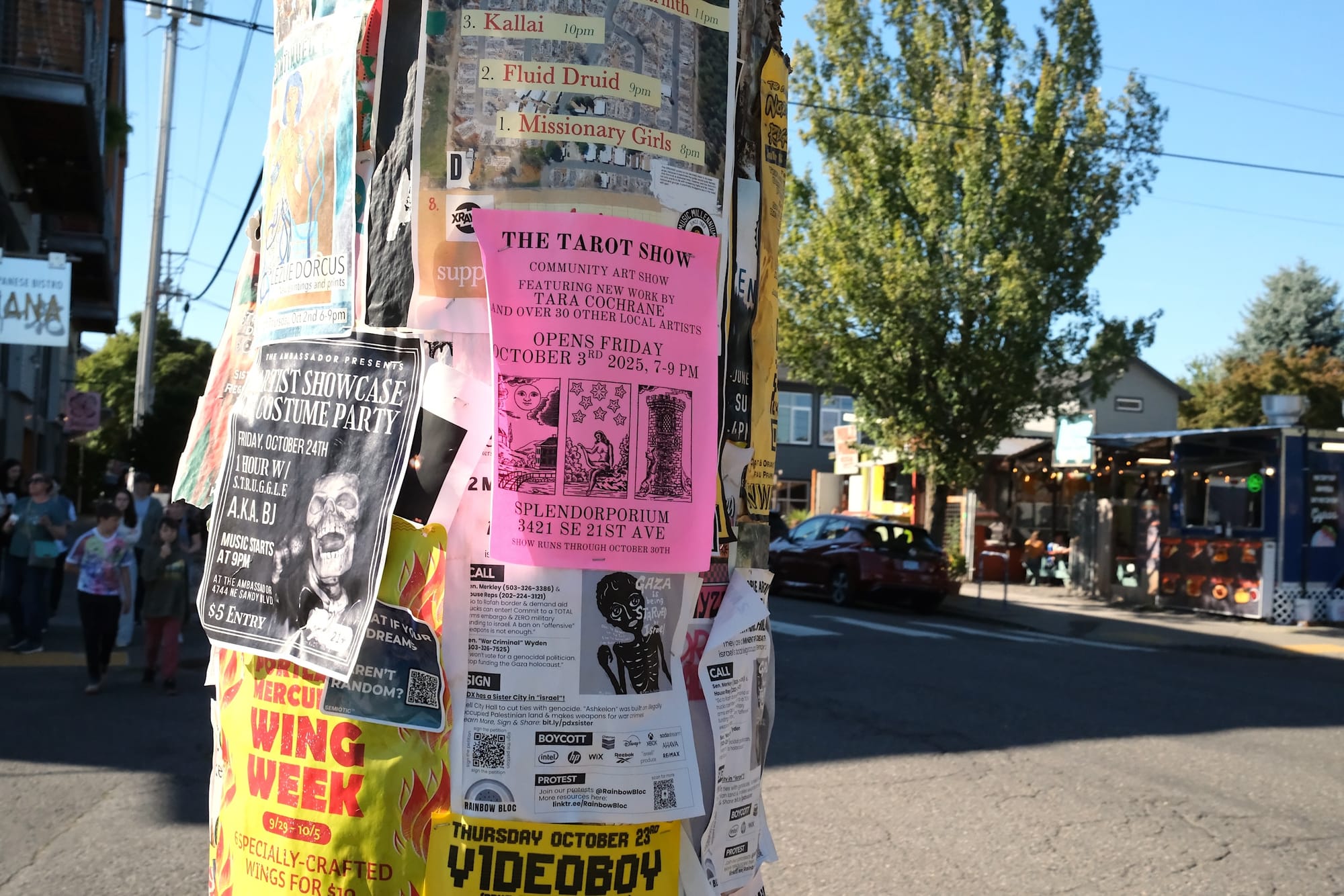 Dozens of posters on a utility pole, including one advertising a tarot community art show.