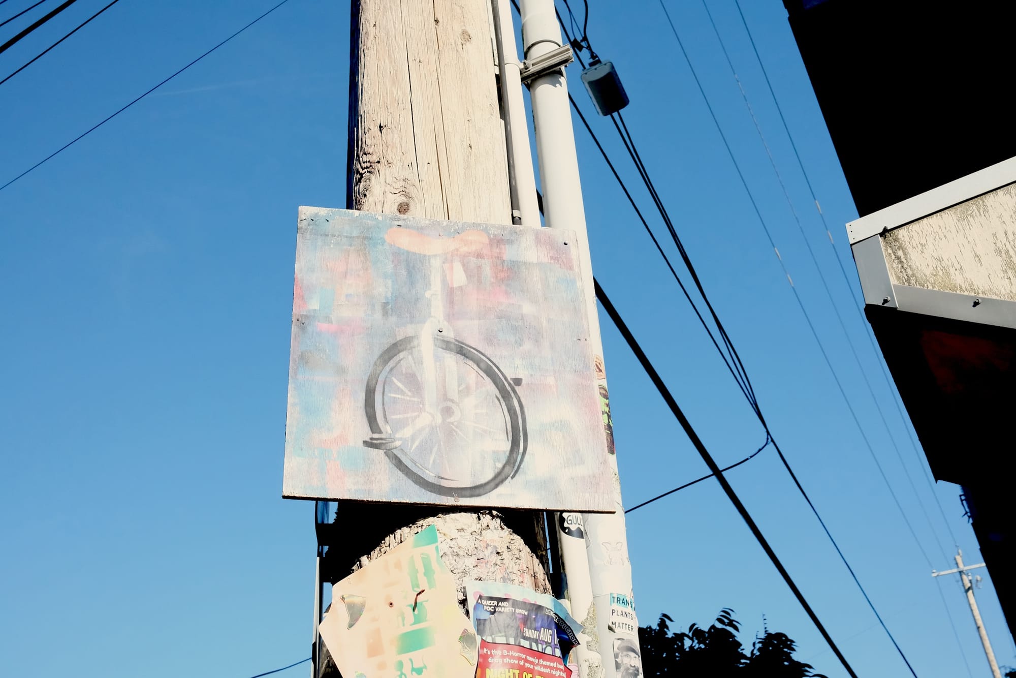 A sign painted with a unicycle screwed to a utility pole.