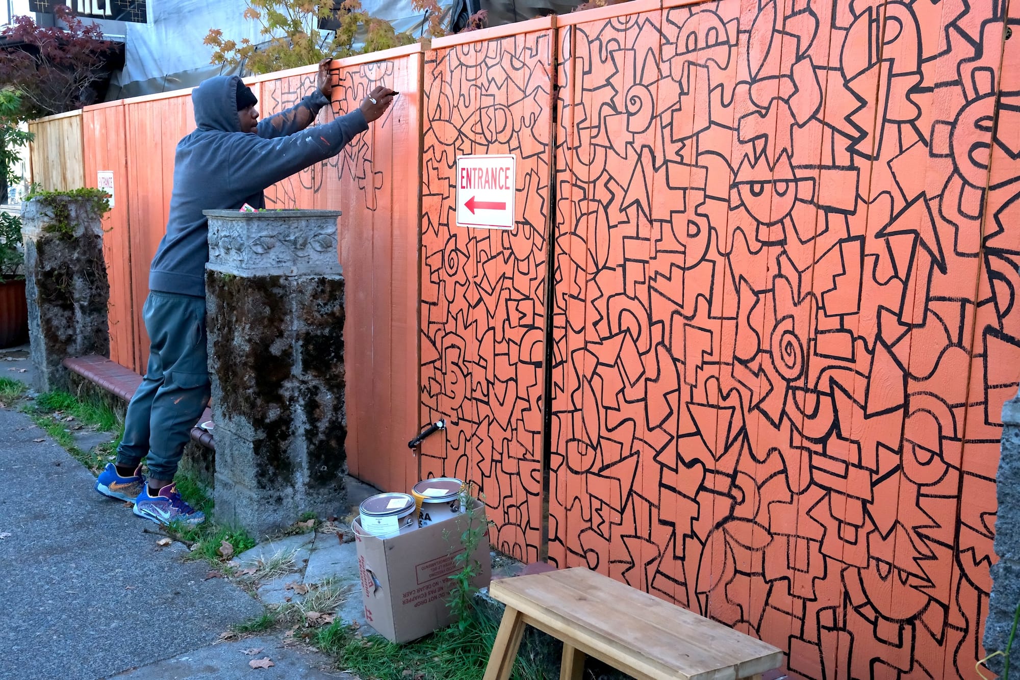An artist paints a mural on a fence.