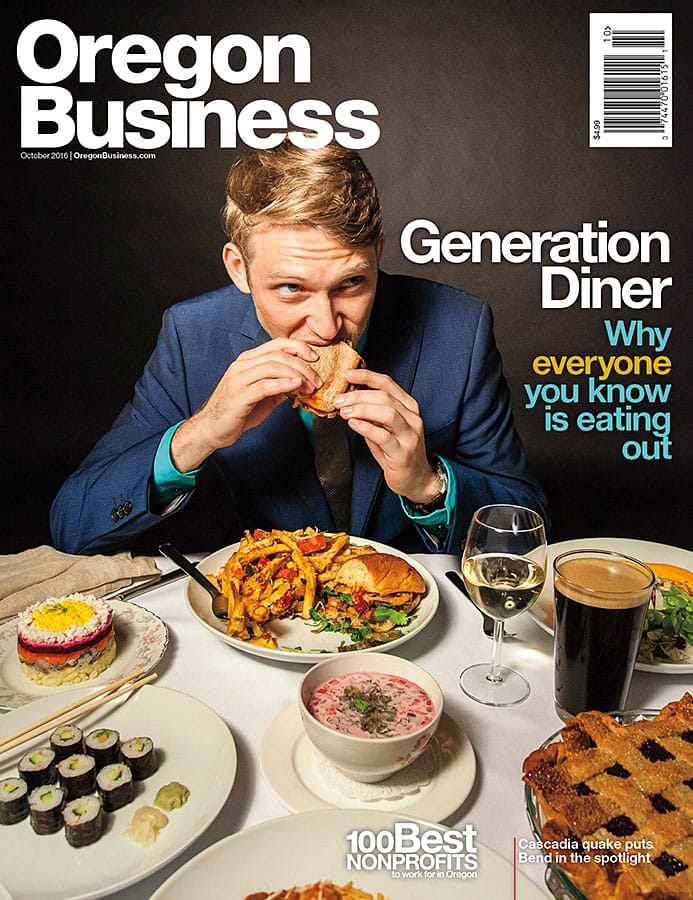 Cover of Oregon Business showing a person in a suit eating a sandwich, while seated at a table covered in delicacies from Oregon.