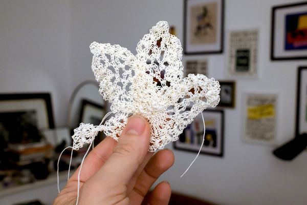 Hand holding delicate white lace bird pin against gallery wall background.